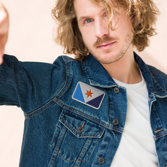 A man wearing a denim jacket with a Syracuse, NY city flag embroidered patch affixed above the right breast pocket
